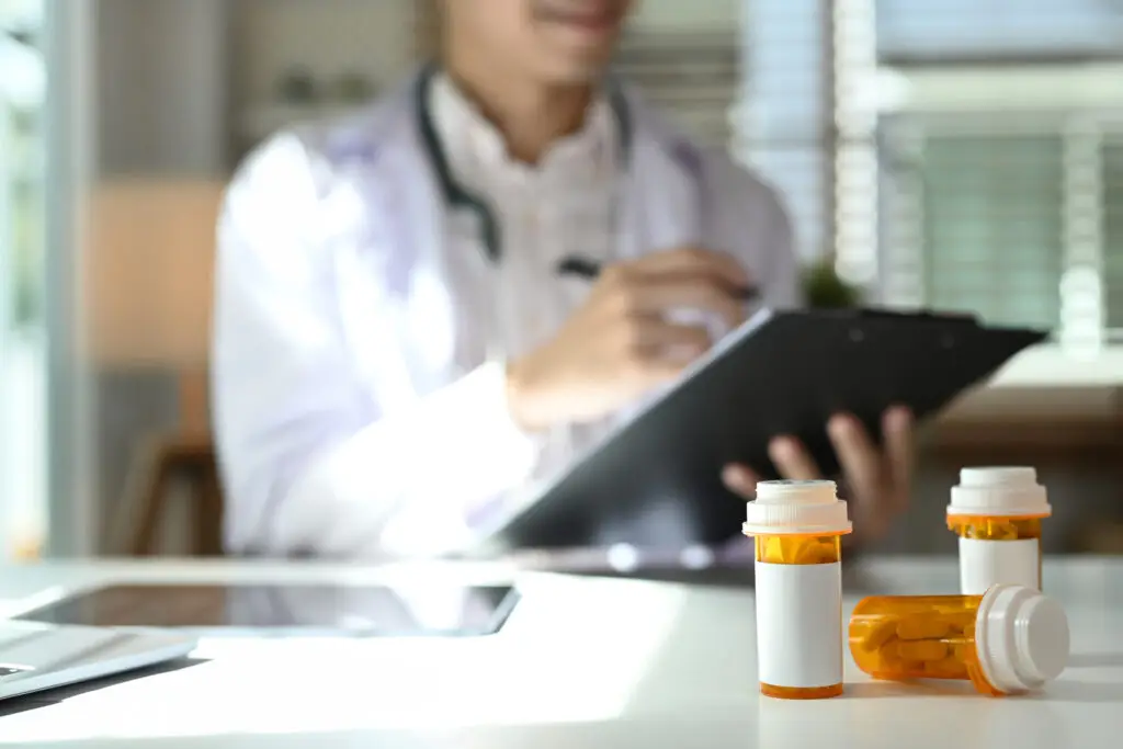 Medical pill bottles with blank label on white table and female doctor sitting in background.